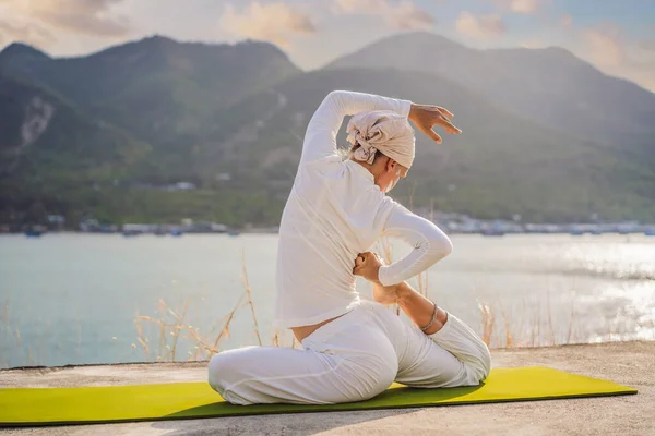 Kundalini Yoga Frau in weißer Kleidung und Turban praktiziert Yoga Kundalini vor dem Hintergrund des Meeres, der Berge und des Sonnenuntergangs. Das kämpferische Kinderschminken der Indianer zeigt ihre innere Welt. Optisch — Stockfoto