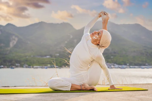 Kundalini Yoga Frau in weißer Kleidung und Turban praktiziert Yoga Kundalini vor dem Hintergrund des Meeres, der Berge und des Sonnenuntergangs. Das kämpferische Kinderschminken der Indianer zeigt ihre innere Welt. Optisch — Stockfoto