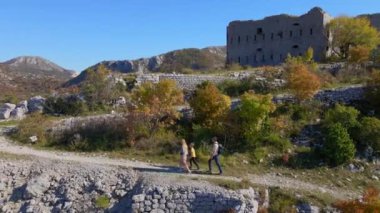 Hava görüntüsü. Dron, Karadağ 'daki Kosmach Kalesi' ne doğru giden bir erkek kadın ve oğullarının ailesini izliyor. Avusturyalılar tarafından savunma amaçlı inşa edilmiş eski bir kale.