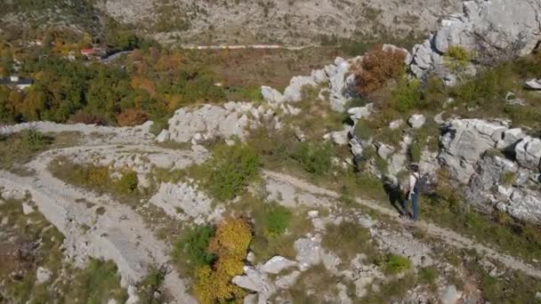Tiro aéreo. Drone segue o homem enquanto ele desce a colina longe da Fortaleza Kosmach em Montenegro. Uma antiga fortaleza construída pelos austríacos como uma estrutura defensiva e um ponto de vista — Vídeo de Stock