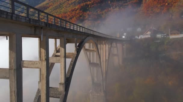 Αεροφωτογραφία της υπέροχης γέφυρας Ντιούρτζεβιτς πάνω από το φαράγγι του ποταμού Τάρα στο βόρειο τμήμα του Μαυροβουνίου. Όμορφη πρωινή ομίχλη κινείται μέσα από τις καμάρες της γέφυρας. Πυροβολήθηκε την φθινοπωρινή περίοδο — Αρχείο Βίντεο