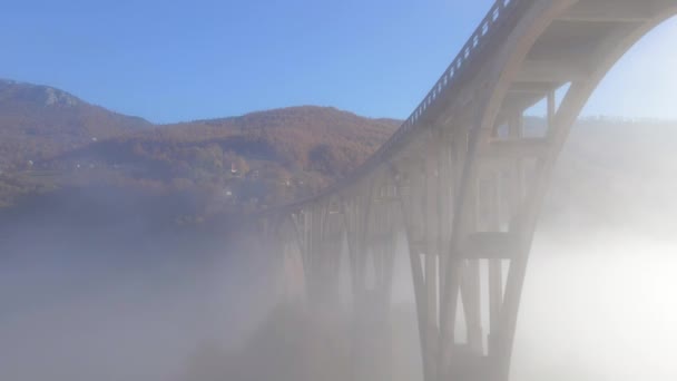 Flygfilm över den magnifika Djurdjevica-bron över Taraflodens kanjon i norra delen av Montenegro. Vacker morgondimma rör sig genom brons valv. Skjuten under höstsäsongen — Stockvideo