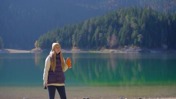 Молодая женщина посещает Crno jezero или Черное озеро недалеко от города Жабляк. Она пьет горячий напиток из термоса, стоящего у озера. Путешествие в Северную Черногорию — стоковое видео