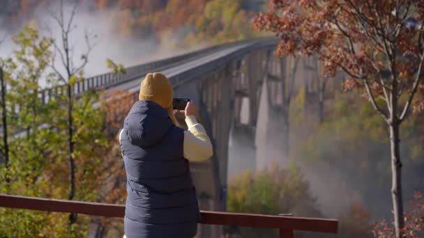 モンテネグロ北部のタラ川渓谷に架かる壮大なジュルジェヴィツァ橋を訪れる女性観光客。秋の季節に撮影。東ヨーロッパの概念への旅行 — ストック動画