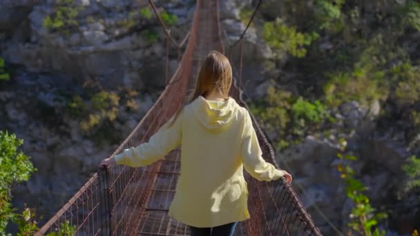 En gammal metallbro över Moracafloden i Montenegro. En kvinna turist i en gul jacka går längs bron — Stockvideo