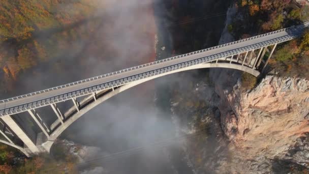 Letecké video velkolepého mostu Djurdjevica přes kaňon řeky Tara v severní části Černé Hory. Krásná ranní mlha se pohybuje oblouky mostu. Shot in the autumn season — Stock video