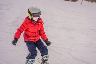 Çocuk dağlarda kayak yapıyor. Güvenlik kaskı, gözlüğü ve direkleri olan aktif bir çocuk. Küçük çocuklar için kayak yarışı. Aile için kış sporu. Alp okulunda çocuklar kayak dersi alıyor. Küçük kayakçı karda yarışıyor