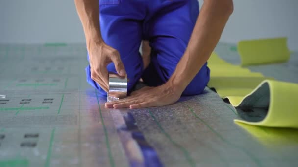 Seorang ahli instalasi pemanas bawah lantai profesional sedang meletakkan dan merekatkan isolasi lantai, di mana ia kemudian akan meletakkan laminasi — Stok Video