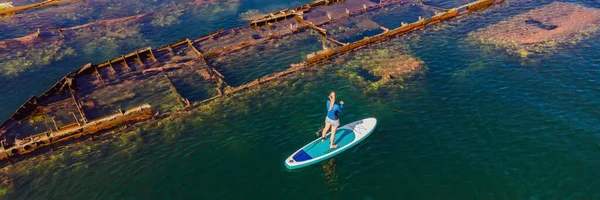 Mujer en tabla de paddle, cenar al lado de naufragio roto abandonado que sobresale del mar BANNER, FORMATO LARGO — Foto de Stock