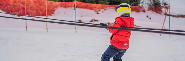 BANNER, LONG FORMAT Boy gyakorló liftet használ. Gyerek síelés a hegyekben. Aktív kisgyerek biztonsági sisakkal, védőszemüveggel és botokkal. Sífutás kisgyerekeknek. Téli sport a családnak. Gyerekek sílecke — Stock Fotó