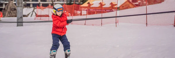 BANNER, LONG FORMAT Boy utilise un ascenseur d'entraînement. Ski d'enfant en montagne. Enfant tout-petit actif avec casque de sécurité, lunettes et bâtons. Course de ski pour jeunes enfants. Sport d'hiver pour la famille. Cours de ski pour enfants — Photo