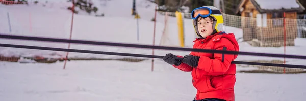 BANNER, LONG FORMAT Boy использует тренировочный подъемник. Дети катаются в горах. Активный ребенок с защитным шлемом, очками и шестом. Лыжная гонка для маленьких детей. Зимний спорт для семьи. Детский урок катания — стоковое фото