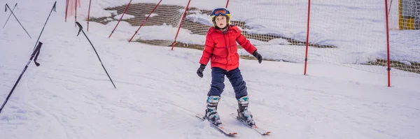 BANNER, LONG FORMAT Barnskidåkning i fjällen. Aktivt småbarn med skyddshjälm, skyddsglasögon och stolpar. Skidtävling för små barn. Vintersport för familjen. Barnens skidlektion i alpin skola. Liten — Stockfoto