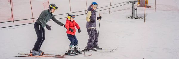 БЕННЕР, ЛОНГ ФОРМАТ Мама и сын учатся кататься на лыжах с инструментарием. Активный ребенок с защитным шлемом, очками и шестом. Лыжная гонка для маленьких детей. Зимний спорт для семьи. Детский урок катания — стоковое фото