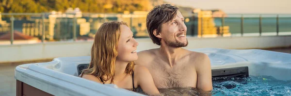 BANNER, FORMATO LARGO Retrato de la joven y despreocupada feliz pareja sonriente relajarse en la bañera de hidromasaje durante el disfrute de la vida feliz momento de viaje de vacaciones en el fondo de grandes montañas verdes — Foto de Stock