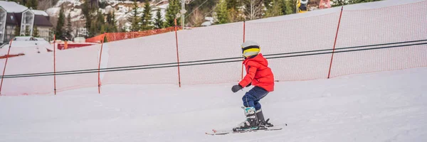 BANNER, FORMATO LARGO Esquí infantil en las montañas. Niño activo con casco de seguridad, gafas y bastones. Carrera de esquí para niños pequeños. Deportes de invierno para la familia. Clases de esquí para niños en la escuela alpina. Pequeño —  Fotos de Stock