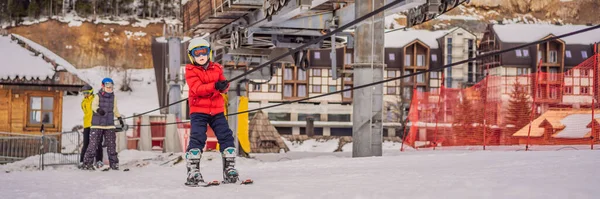 BANNER, LONG FORMAT Boy uses a training lift. Child skiing in mountains. Active toddler kid with safety helmet, goggles and poles. Ski race for young children. Winter sport for family. Kids ski lesson — Stock Photo, Image