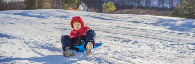 Banner, uzun zamandır mutlu ve pozitif olan küçük çocuk kızak ve soğuk havanın tadını çıkarıyor, kış eğlencesi konsepti.
