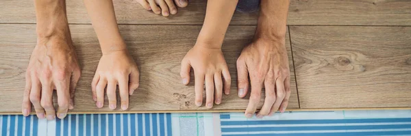 BANNER, LONG FORMAT Father and son installing new wooden laminate flooring on a warm film floor. Infrared floor heating system under laminate floor — Stock Photo, Image