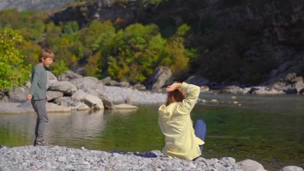 Een vrouw en haar zoon ontspannen aan de oever van de rivier en gooien stenen in de rivier de Moracha. Reizen naar Montenegro — Stockvideo