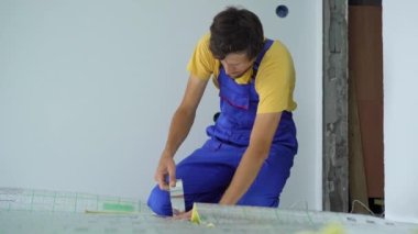 Profesyonel bir yer altı ısıtma tesisatı ustası zemine yalıtım malzemelerini yapıştırıyor.