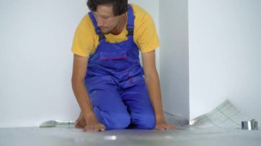Profesyonel bir yer altı ısıtma tesisatı ustası zemine yalıtım malzemelerini yapıştırıyor.
