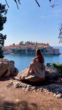 Dikey video. Genç kadın Sveti Stefan adası yakınlarındaki parkı ziyaret ediyor. Budva şehrinin yakınlarında ünlü bir turistik mekan. Karadağ 'a Seyahat
