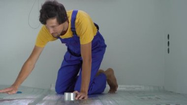 Profesyonel bir yer altı ısıtma tesisatı ustası zemine yalıtım malzemelerini yapıştırıyor.