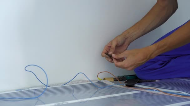 Profesjonalny mistrz instalacji ogrzewania podłogowego łączy folię grzewczą na podczerwień z obwodem elektrycznym. Strzał z bliska — Wideo stockowe