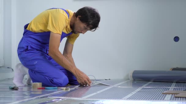 A professional master of underfloor heating installation connects the infrared heating film to the electric circuit — Stock Video