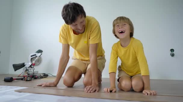 Отец и его маленький сын устанавливают ламинат на полу в своей квартире. Концепция DIY — стоковое видео