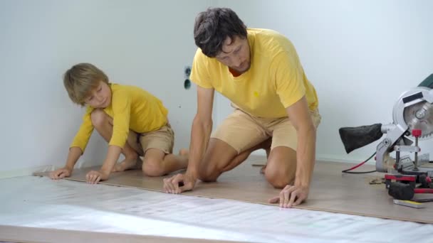 Vater und kleiner Sohn verlegen Laminat auf dem Fußboden in ihrer Wohnung. DIY-Konzept — Stockvideo