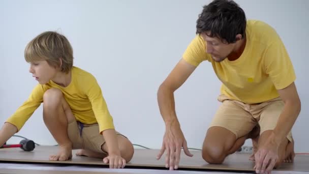 Vader en zijn zoontje leggen laminaat op de vloer in hun appartement. DIY-concept — Stockvideo