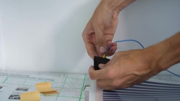 床下暖房設置のプロのマスターは、赤外線加熱フィルムを電気回路に接続します。閉鎖ショット。 — ストック動画