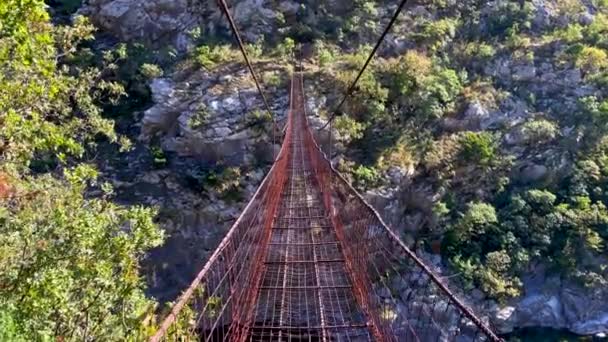 Video di punto di vista. Scatto al rallentatore di una persona che cammina lungo il vecchio ponte di corda metallica attraverso il canyon del fiume Moraca in Montenegro — Video Stock