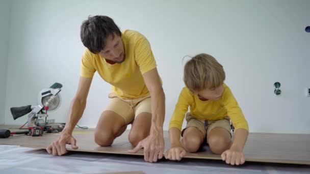 Отец и его маленький сын устанавливают ламинат на полу в своей квартире. Концепция DIY — стоковое видео