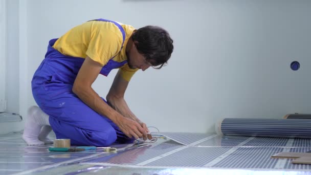 A professional master of underfloor heating installation connects the infrared heating film to the electric circuit — Stock Video