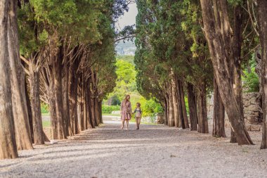 Karadağ 'da anne ve oğul turistler birlikte yürüyor. Karadağ 'ın Adriyatik Denizi kıyısındaki güzel yeşil Kraliyet Parkı Milocer' in panoramik yaz manzarası