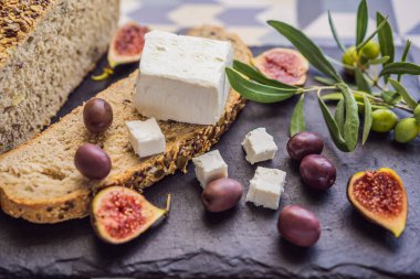 Yeşil ve siyah zeytinli somun taze ekmek, feta peyniri ve zeytin dalları koyu arkaplan üzerine zeytin ağacı doğrama tahtası