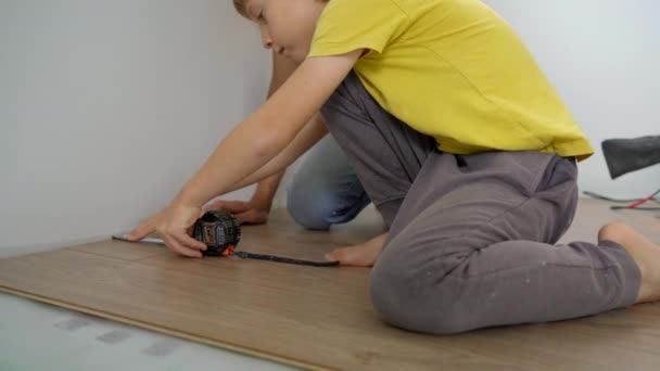 Батько і його маленький син встановлюють ламінат на підлогу у своїй квартирі. Концепція DIY — стокове відео