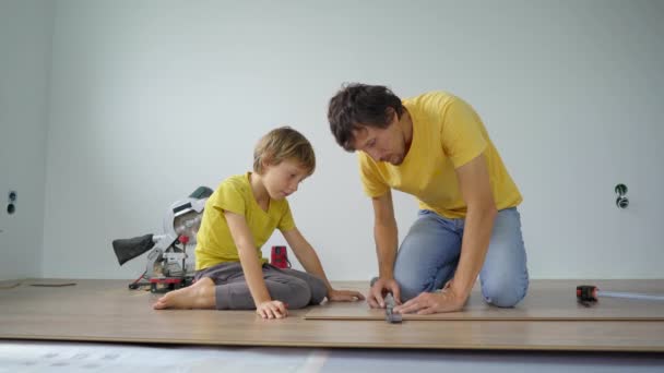 Vater und kleiner Sohn verlegen Laminat auf dem Fußboden in ihrer Wohnung. DIY-Konzept — Stockvideo