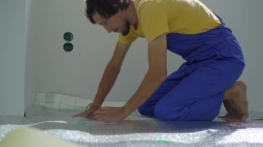 Profesyonel bir yer altı ısıtma tesisatı ustası zemine yalıtım malzemelerini yapıştırıyor.