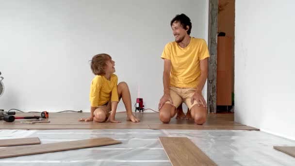 Far och hans son installerar laminat på golvet i deras lägenhet. Gör det själv. Långsamma rörelser video — Stockvideo