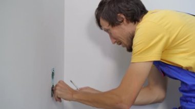 Bir elektrikçi duvara elektrik prizi takıyor. İnşaat ve ev onarımı
