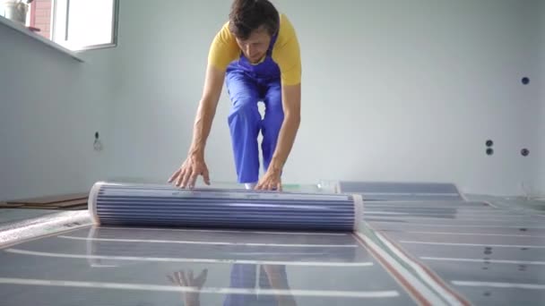 Profesionální mistr v instalaci podlahového vytápění rozkládá infračervený topný film — Stock video