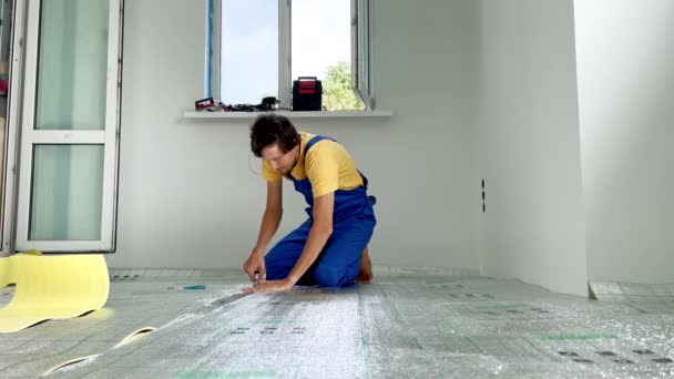 床下暖房設置のプロのマスターがレイアウトされており、彼はその後、ラミネートを置く床のための断熱材を接着しています。スローモーションビデオ — ストック動画