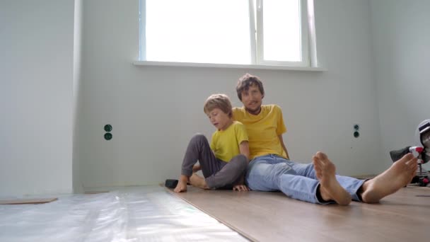 Батько і його маленький син встановлюють ламінат на підлогу у своїй квартирі. Концепція DIY — стокове відео