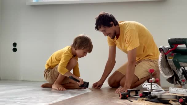 Vader en zijn zoontje leggen laminaat op de vloer in hun appartement. Doe-het-zelf concept. Langzame video — Stockvideo