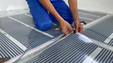Yavaş çekim videosu. Yeraltı ısıtma kurulumunda profesyonel bir usta kızılötesi ısıtma filmini elektrik devresine bağlar. Yakın çekim.