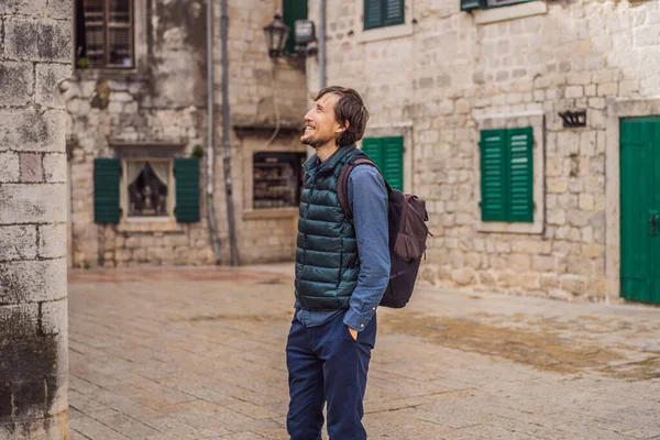 Karadağ 'ın eski Kotor kasabasında güneşli bir günde renkli caddenin tadını çıkaran erkek turist. Karadağ 'a Seyahat